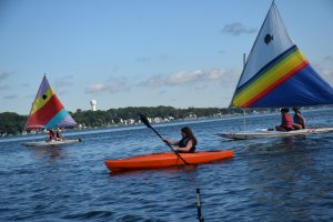female camper paddling in kayak and other campers on sailboats behind her