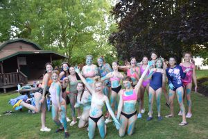 female campers posing for the camera in the bathing suits with blue paint all over themselves.